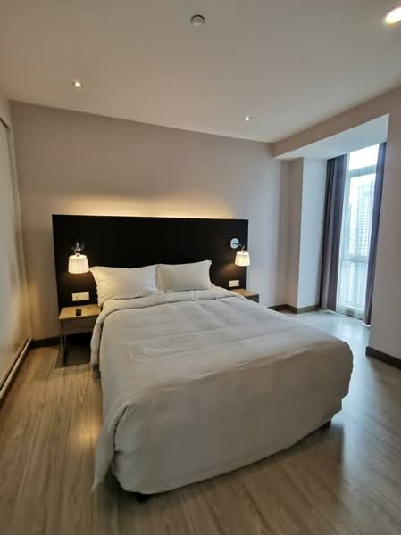Bedroom features: queen-size bed with white bedding, two bedside lamps, wooden bedside tables, dark accent wall behind the bed, large window with sheer curtains, wooden flooring, recessed ceiling lights, wall-mounted light fixtures; style: modern; view: city.