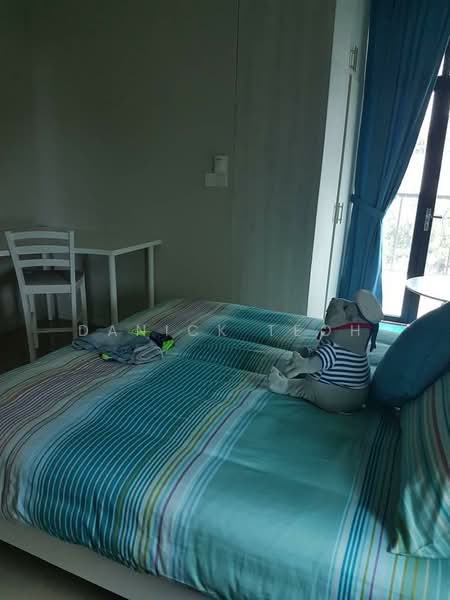 Bedroom features: queen-size bed with striped bedding, upholstered headboard, decorative cushions, wooden chair, small dining table, floor-to-ceiling window, blue curtains, light-colored walls, laminate flooring, stuffed toy on bed; style: modern.