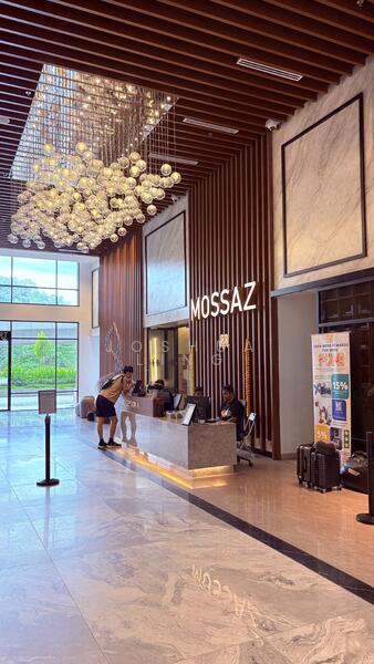 Lobby features: chandelier with multiple glass globes, wooden feature wall with horizontal slats, marble flooring with polished finish, reception desk with stone countertop, large windows allowing natural light, seating area with modern chairs, decorative wall art, luggage trolleys, information banners, high ceiling with wooden beams; style: modern; view: garden.