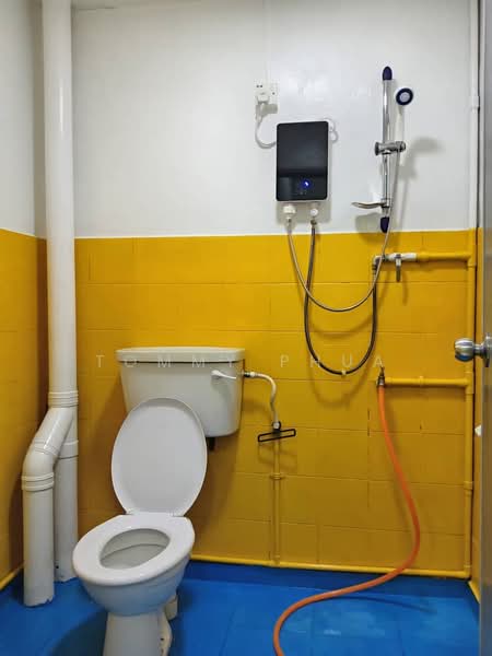 Bathroom features: yellow tiled walls, white toilet, shower with handheld showerhead, blue vinyl flooring, exposed plumbing, wall-mounted water heater, orange hose, white flush tank.
