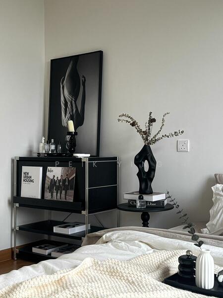 Bedroom features: white painted walls, light-colored bedding, black and white artwork on wall, metal side table, decorative vase with dried flowers, black sculpture, shelf with books and decorative items, soft throw blanket; style: modern.