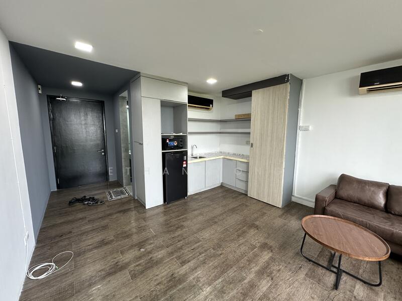 Living features: laminate flooring, grey painted walls, exposed concrete wall, 2-seater brown leather sofa, round wooden coffee table, wall-mounted air conditioning unit, recessed LED downlights, open kitchen layout, kitchen cabinetry, microwave, mini fridge, kitchen countertop; style: modern.