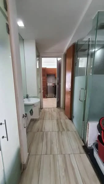 Room features: light-colored tiled flooring, white walls, glass shower enclosure, single-bowl sink, wood cabinetry, refrigerator visible in background, door leading to another room, open hallway layout; style: modern.