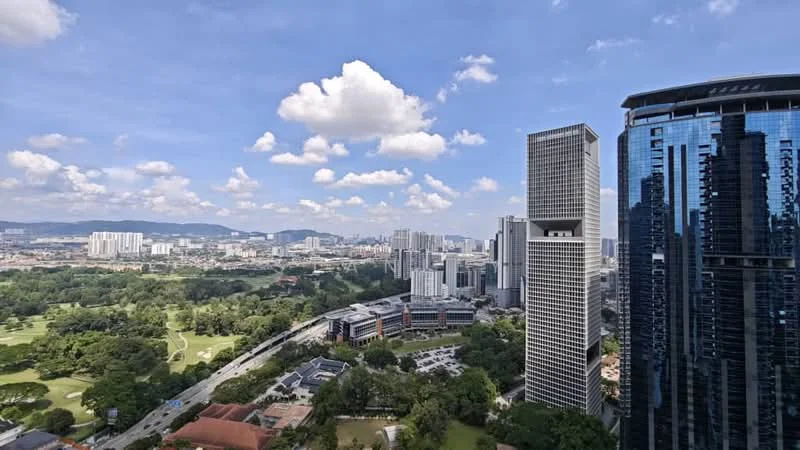 Exterior type: high-rise condominium; features: glass curtain wall, surrounded by greenery, city skyline view, manicured lawn, urban landscape, adjacent to highway; style: modern.