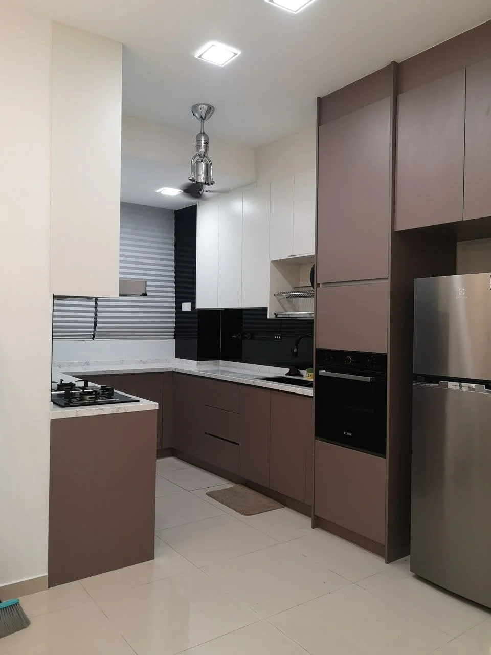 Kitchen features: L-shaped kitchen layout, white upper cabinets, brown lower cabinets, granite countertop, stainless-steel sink, chrome pull-down faucet, built-in oven, stainless-steel fridge, 4-burner gas hob, exhaust hood, tile backsplash, recessed LED downlights, window with blinds, floor tiles, kitchen island with seating; style: modern.