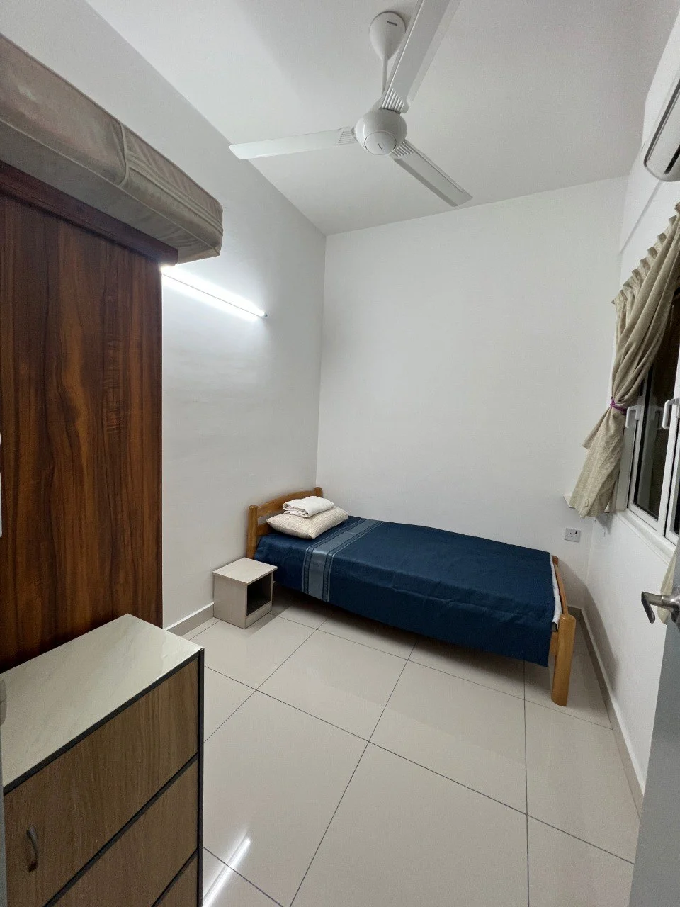 Bedroom features: single bed with blue bedding, wooden bed frame, white painted walls, glossy tile flooring, ceiling fan, window with curtains, wooden wardrobe, nightstand; style: modern.