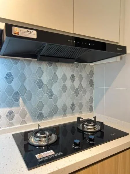 Kitchen features: black glass cooktop, 2-burner gas hob, stainless-steel knobs, black range hood, hexagonal tile backsplash, light-colored countertop, wood cabinetry, under-cabinet lighting; style: modern.