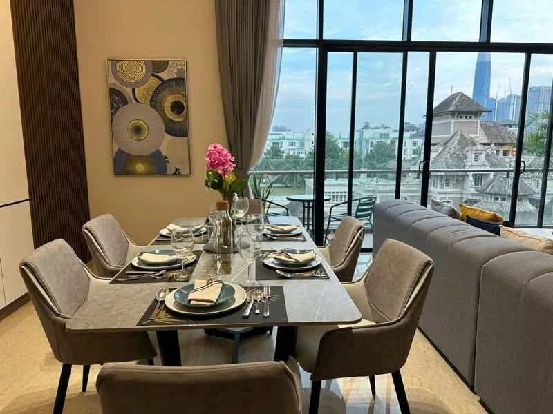 Dining features: 6-seater dining table with marble top, upholstered dining chairs in grey, decorative vase with flowers, table setting with plates and cutlery, framed artwork on wall, large windows with city view, curtains, light-colored walls, tile flooring; style: modern; view: city. Living features: L-shape sectional sofa in grey, coffee table, decorative cushions, floor-to-ceiling windows, light-colored walls, tile flooring; style: modern; view: city.