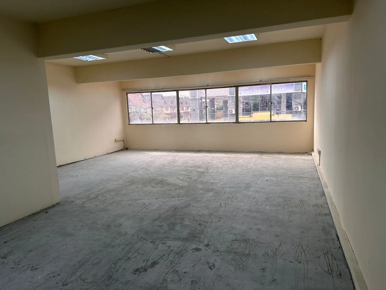 Room features: plain beige painted walls, concrete flooring, large windows, multiple ceiling lights, wall-mounted air conditioning units; style: minimalist; view: city.