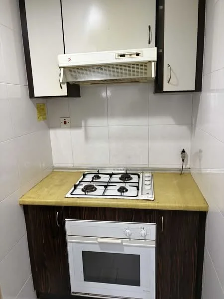 Kitchen features: white tiled walls, brown wooden cabinetry, cream countertop, built-in oven in white, 4-burner gas hob, exhaust hood, single-bowl stainless-steel sink, wall-mounted electrical outlet; style: modern.