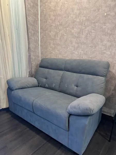 Living features: grey fabric 2-seater sofa, textured wall with neutral color, dark wood flooring, sheer curtains, corner table; style: modern.