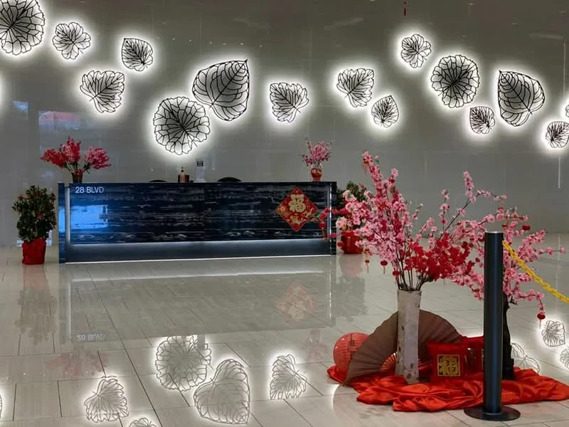 Room features: reception desk, backlit decorative wall with floral patterns, marble flooring, red decorative flowers in pots, red fabric draping, decorative fan, Chinese New Year decorations, reflective surfaces; style: modern.