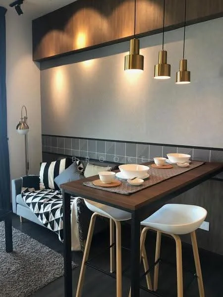 Dining features: wooden dining table, black metal legs on table, gold pendant lights, white bar stools, black and white patterned throw blanket, grey upholstered sofa, textured wall paneling, decorative wall shelf, ceramic dinnerware, area rug with soft texture; style: modern.
