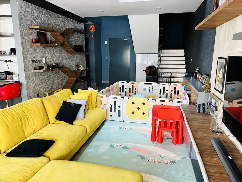 Living features: yellow fabric sectional sofa, black throw pillows, wooden shelving unit with decorative items, grey accent wall with stone texture, wooden staircase, playpen with colorful panels, children's plastic chair and table, flat-screen TV on wooden console, area rug with playful design, recessed lighting, large windows for natural light; style: modern. Kitchen features: red bar stools, kitchen island, open layout, stainless-steel appliances; style: modern.
