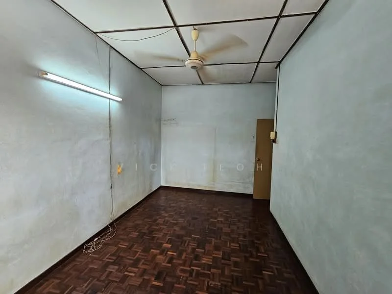 Room features: light blue painted walls, parquet wood flooring, ceiling fan, fluorescent light fixture, single wooden door, exposed ceiling tiles, no visible windows, empty space.