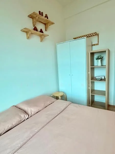 Bedroom features: queen-size bed with beige bedding, light wood shelving unit on wall, white wardrobe with sliding doors, wooden stool, decorative shelf with items, light wood bookshelf, green potted plant, cream painted walls, wooden flooring; style: minimalist.
