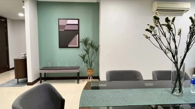 Dining features: glass dining table, upholstered dining chairs, green accent wall, white painted walls, wall-mounted air conditioning unit, decorative plant in pot, framed artwork on wall, side table, water bottle on table; style: modern.
