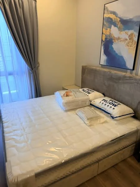 Bedroom features: queen-size bed, upholstered headboard, bedside table, decorative pillows, bedding with protective covering, floor-to-ceiling window, sheer curtains, wooden flooring, framed artwork on wall; style: modern.