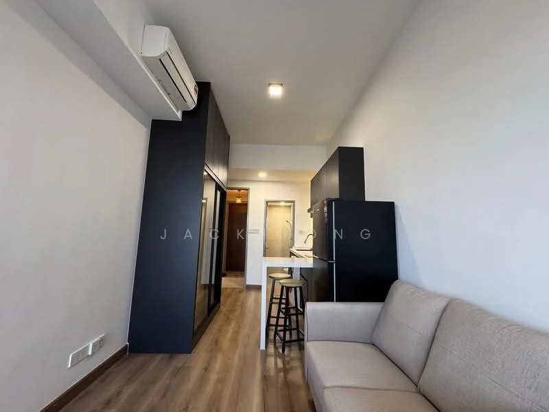 Living features: light grey fabric sofa, wooden flooring, wall-mounted split AC, recessed ceiling lights, open layout, bar stool, black refrigerator, kitchenette with countertop, neutral painted walls, doorway leading to hallway; style: modern.