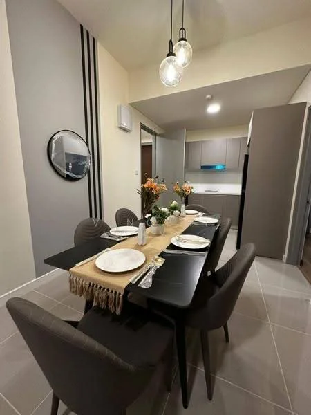 Dining features: 6-seater dining table, black dining table, upholstered dining chairs in grey, decorative table runner, vase with flowers, wall-mounted mirror, pendant lighting with glass bulbs, air conditioning unit on wall, grey accent wall with vertical stripes, light grey tiled flooring; style: modern. Kitchen features: kitchen cabinetry in light grey, countertop with integrated sink, built-in kitchen appliances, open layout to dining area; style: modern.