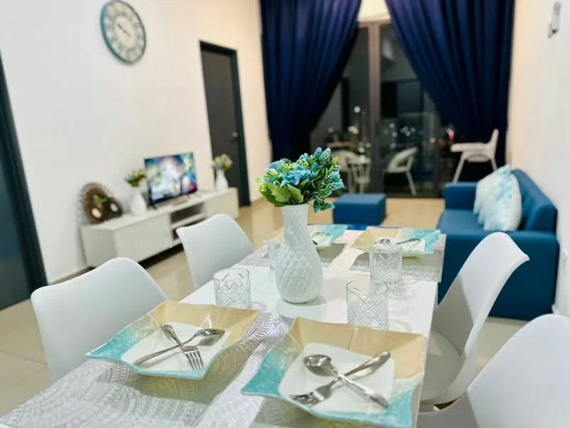 Dining features: white dining table, 4 white dining chairs, decorative table runner, blue and beige plates, cutlery on plates, glass drinking glasses, white vase with flowers, wall clock, floor-to-ceiling windows, blue curtains, light-colored tiled flooring; style: modern; view: city. Living features: blue fabric sofa, white TV console, wall-mounted TV, decorative wall art, light-colored tiled flooring; style: modern; view: city.