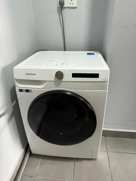 Laundry features: white front-load washing machine, grey tiled flooring, light grey painted walls, power outlet on wall.