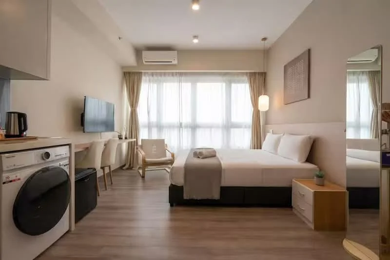 Bedroom features: queen-size bed, upholstered headboard, bedside table, wall-mounted TV, floor-to-ceiling windows, sheer curtains, wooden flooring, recessed downlights, air conditioning unit, mirror, laundry machine, kettle, dining table with chairs; style: modern.