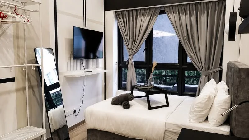 Bedroom features: queen-size bed with white bedding, upholstered headboard, two white pillows, black bedside table, decorative vase on bedside table, grey curtains, floor-to-ceiling windows, wall-mounted TV, mirror on stand, clothing rack, wooden flooring, light fixture, decorative towels; style: modern; view: garden.