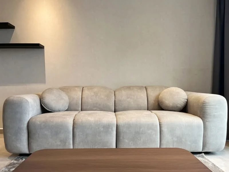 Living features: 3-seater fabric sofa in light grey, two round cushions, wooden coffee table, plain wall in neutral colour, shelf unit on wall; style: modern.