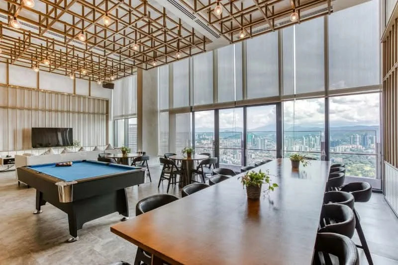Room features: large windows with city view, wooden dining table, black dining chairs, pool table, exposed ceiling with wooden beams, concrete flooring, indirect lighting, potted plants on table, wall-mounted TV, sheer window treatments; style: modern; view: city.