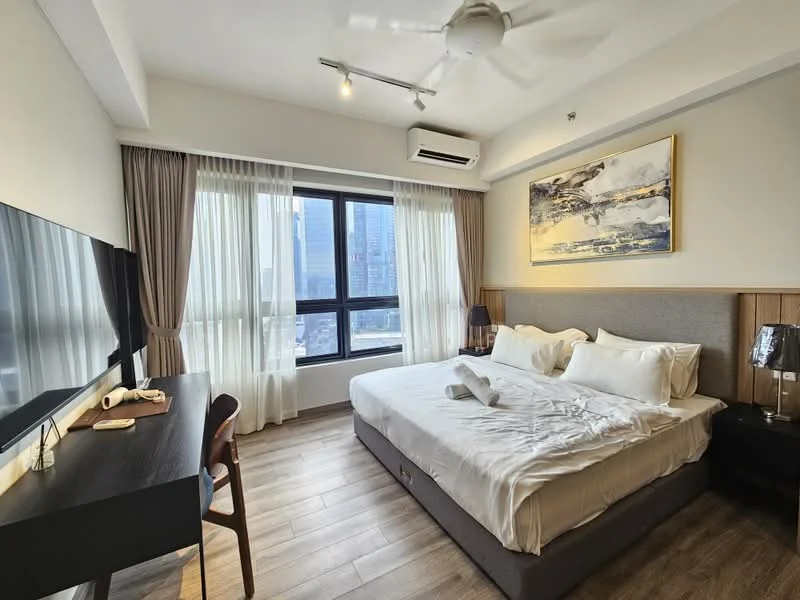 Bedroom features: king-size bed with white bedding, upholstered headboard, 2 bedside lamps, wooden flooring, floor-to-ceiling windows, sheer curtains, blackout curtains, wall-mounted TV, study desk with chair, ceiling fan with light, air conditioning unit, decorative artwork on wall; style: modern; view: city.