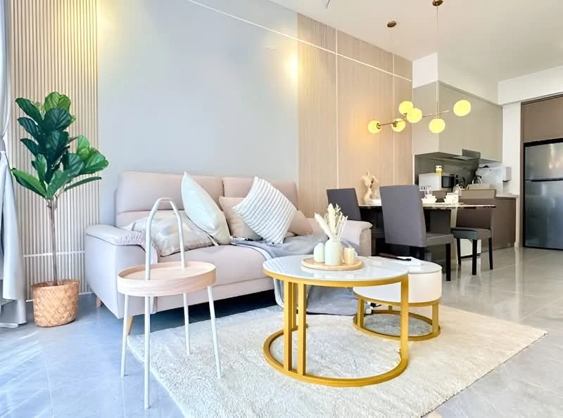 Living features: light grey painted walls, marble tile flooring, 3-seater fabric sofa in light beige, decorative cushions, round coffee table with gold frame, area rug with neutral color, pendant lighting with multiple bulbs, indoor plant in decorative pot, dining table with four grey upholstered chairs, kitchen area visible in background with stainless-steel fridge; style: modern.