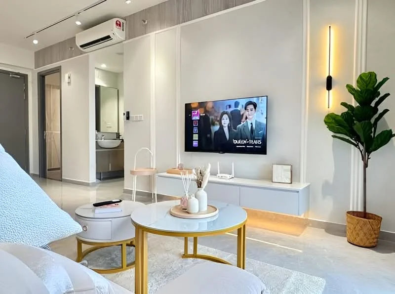 Living features: light grey sofa, round coffee table with white top, flat-screen TV mounted on wall, TV console with storage, decorative plant in pot, wall-mounted light fixture, recessed ceiling lights, marble tile flooring, air conditioning unit, open layout to kitchen area, neutral wall color with wood paneling; style: modern. Room features: mirror in bathroom visible, doorway leading to bathroom.