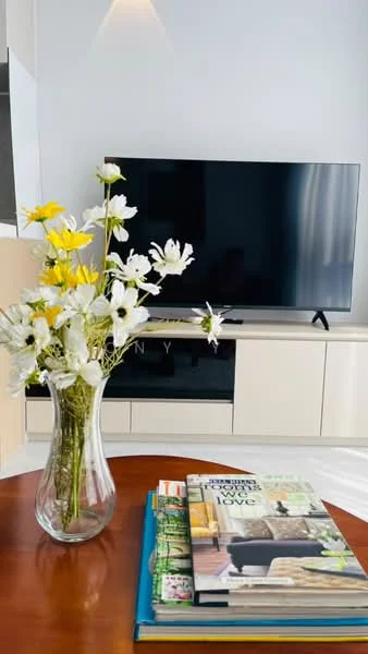 Living features: wall-mounted TV, light wood TV console, decorative vase with flowers, coffee table, magazines on coffee table, neutral wall color, large window with sheer curtains, area rug; style: modern.