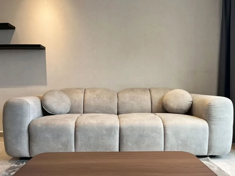 Living features: 3-seater fabric sofa in light grey, two round cushions, wooden coffee table, plain wall in neutral colour, shelf unit on wall; style: modern.