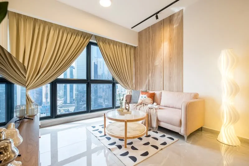Living features: floor-to-ceiling windows, beige fabric sofa, round coffee table, area rug with geometric pattern, wood accent wall, curtains in light beige, decorative floor lamp, marble tile flooring, wall-mounted TV console, decorative plant, city view; style: modern; view: city.
