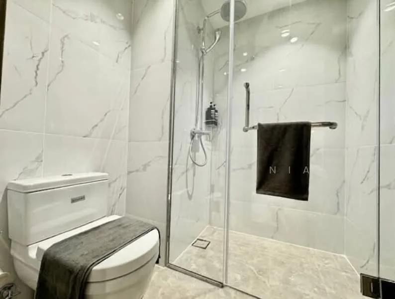 Bathroom features: white one-piece toilet, walk-in shower with glass enclosure, chrome shower head, chrome handheld shower, grey towel hanging on towel rack, marble wall tiles with grey veining, light-colored stone flooring, recessed downlights; style: modern.