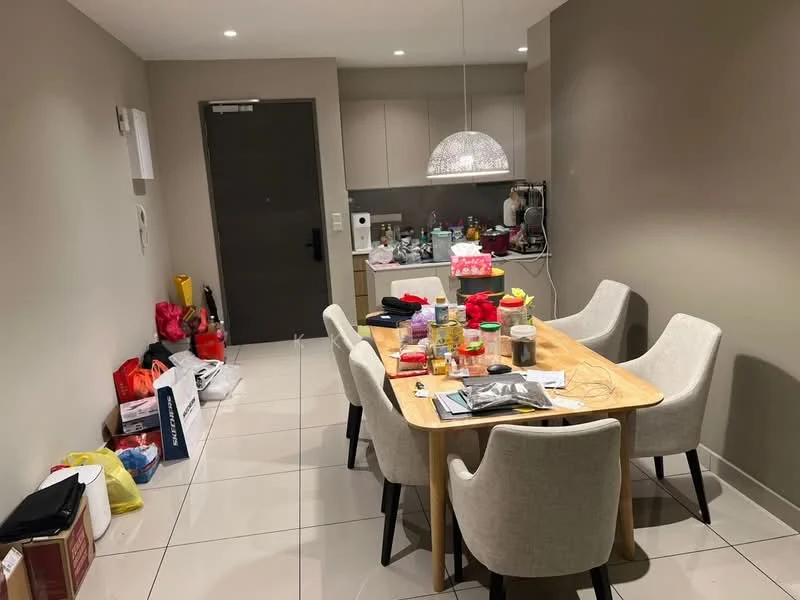 Dining features: rectangular wooden dining table, 4 upholstered dining chairs in light grey, pendant light fixture, white tiled flooring, cream painted walls, kitchen area visible in background, various items on the table, decorative items on the table, open doorway to entrance, wall-mounted intercom, kitchen cabinets visible; style: modern.