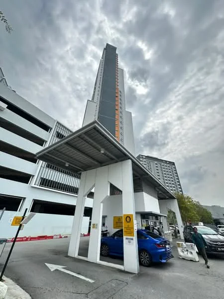 Exterior type: high-rise condominium; features: glass curtain wall, grey painted facade, orange accent panels, covered entrance with awning, multi-storey car park, signage at entrance, surrounded by urban landscape; style: modern.