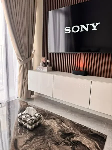 Living features: white TV console, dark wood accent wall, large flat-screen TV, cream curtains, marble flooring, decorative silver spheres, decorative books, LED light on console; style: modern.