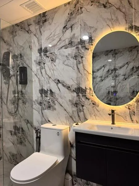 Bathroom features: marble tile walls, white porcelain one-piece toilet, single-sink vanity with dark wood cabinet, chrome basin mixer faucet, framed oval mirror with backlighting, glass shower enclosure, rain shower head, recessed downlights, tile flooring; style: modern.