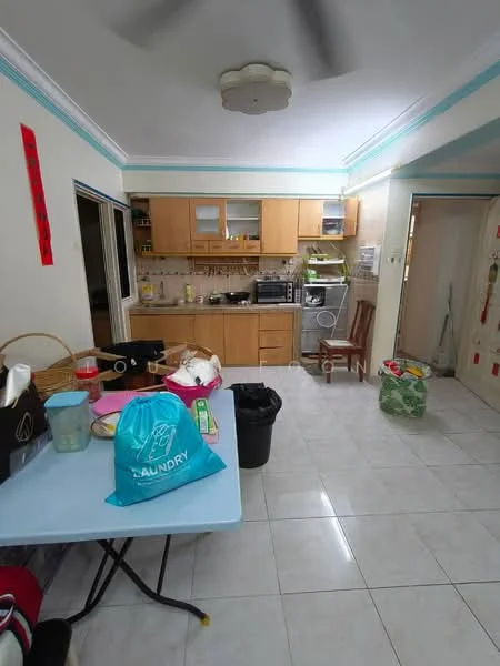 Kitchen features: light-colored wooden cabinetry, ceramic tile flooring, white walls, recessed ceiling lights, ceiling fan, stainless-steel sink, built-in oven, microwave, washing machine, countertop with appliances, open layout to dining area, window with sheer curtains; style: modern. Dining features: blue plastic table, plastic chairs, waste bin, laundry bag, various kitchen items on table.