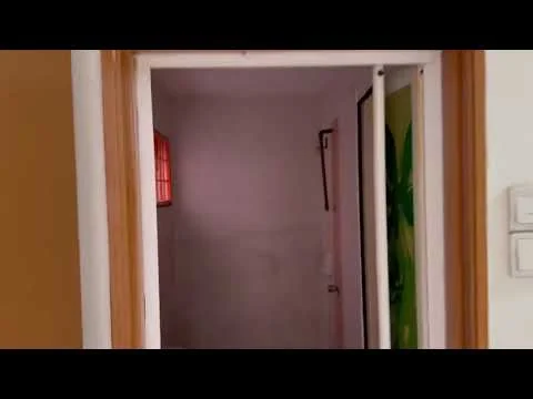 Room features: white painted walls, wooden door frame, light switch, window with red grille, unknown flooring.