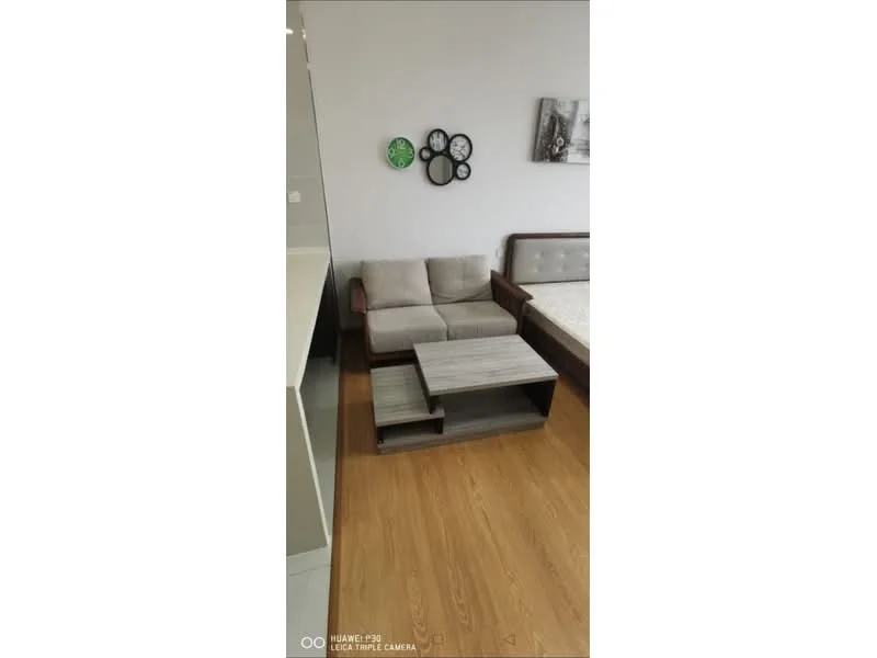 Living features: 3-seater fabric sofa in beige, wooden coffee table with storage, laminate flooring, wall-mounted clock, framed artwork, decorative wall plates, neutral wall color, bed with mattress; style: modern.