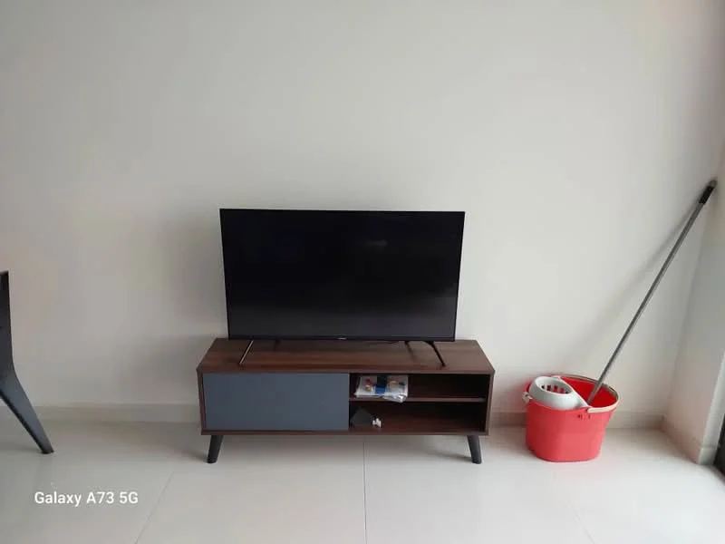 Room features: flat-screen TV on wooden TV console, wooden TV console with grey cabinet door, white painted walls, glossy tile flooring, cleaning bucket, mop, minimalist decor; style: modern.