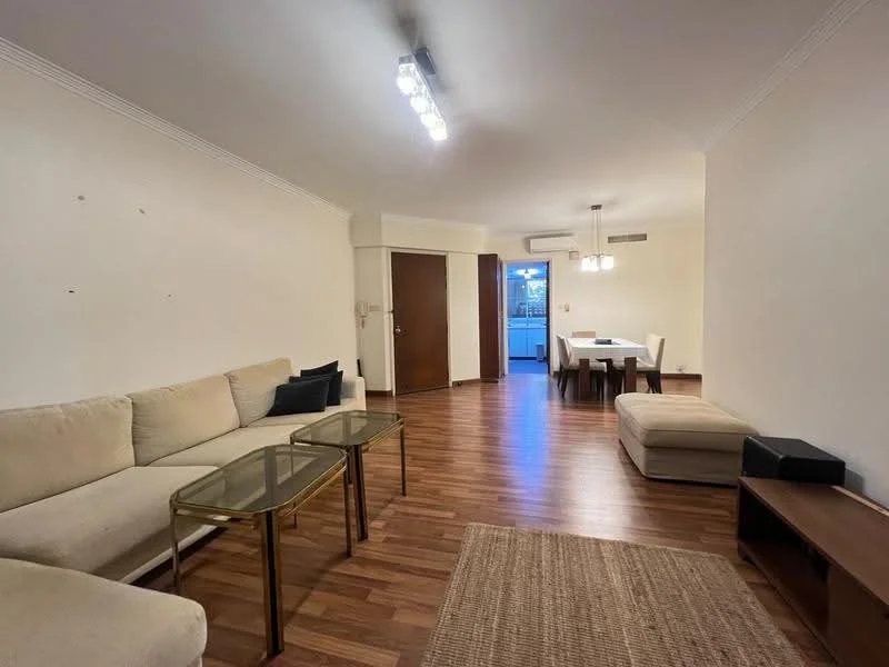 Living features: L-shape sectional sofa in beige, two glass-top coffee tables, wood flooring, recessed LED downlights, wall-mounted air conditioning unit, dining table with chairs visible in background, door leading to outdoor area, decorative area rug; style: modern.