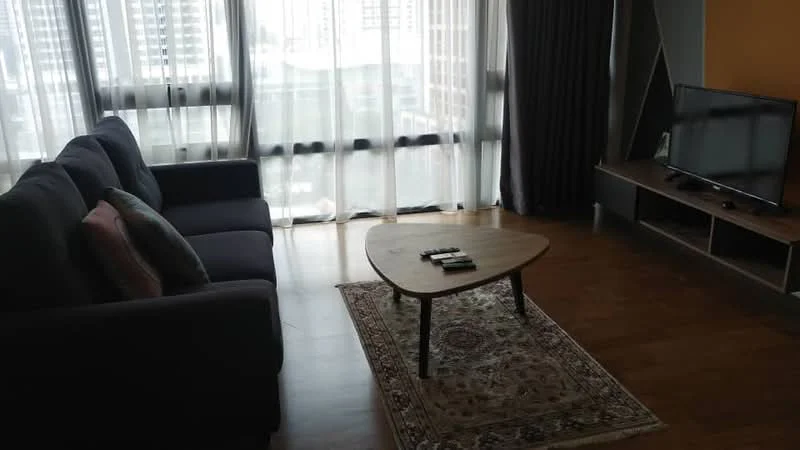 Living features: 3-seater fabric sofa in dark grey, coffee table with wooden surface, area rug with intricate pattern, floor-to-ceiling windows with sheer curtains, wooden flooring, wall-mounted TV, TV console with storage, decorative cushions on sofa; style: modern; view: city.
