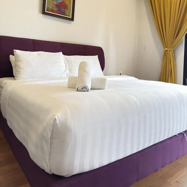 Bedroom features: king-size bed with upholstered headboard, white bedding, purple bed frame, yellow curtains, wooden flooring, framed artwork on wall, two white towels rolled on bed; style: modern.