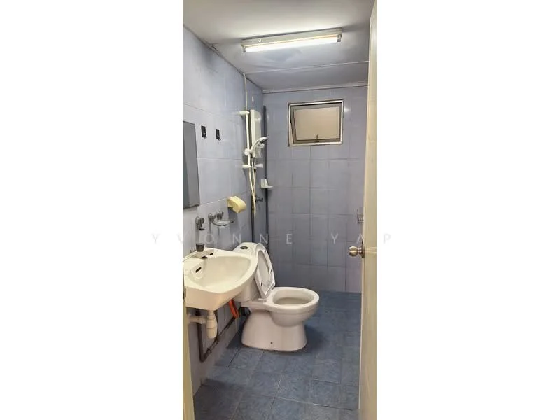 Bathroom features: blue ceramic tile walls, blue ceramic tile flooring, single-sink vanity with white cabinet, chrome basin mixer faucet, toilet, shower with wall-mounted showerhead, window for natural light, towel holder, toilet paper holder, light fixture on ceiling.