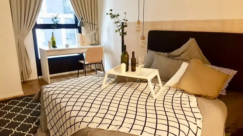 Bedroom features: king-size bed, upholstered headboard, white and grey bedding, decorative throw pillows, bedside tray with glasses and bottles, wooden flooring, floor-to-ceiling window, sheer curtains, desk with chair, decorative plant on desk, area rug with geometric pattern; style: modern; view: city.